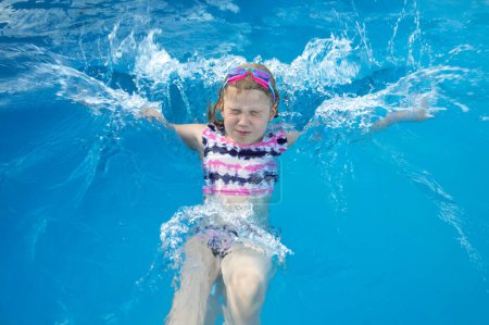 Joyful child splashing into swimming pool in summer in aquapark