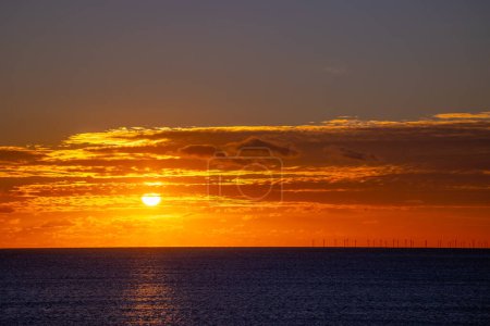 Foto de Puesta de sol sobre el Canal de la Mancha durante diciembre, con turbinas de parque eólico Rampion en el horizonte y sendero iluminado por el sol en el mar. - Imagen libre de derechos