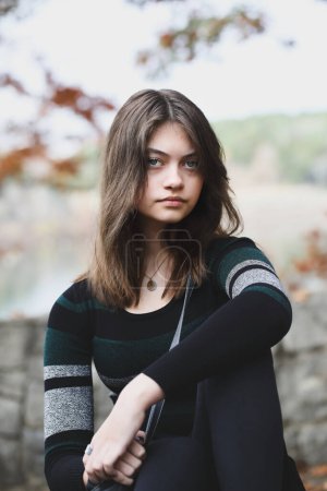 Photo for Beautiful brunette young woman looking into the camera with serious expression surrounded by outdoor autumn colors. Selective focus with blurred background. - Royalty Free Image