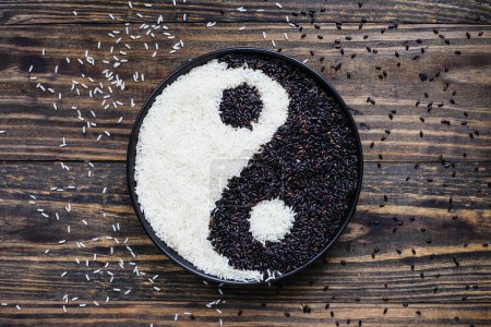 Photo for Nerone rice, organic forbidden black, and Jasmine Rice in a black bowl over wood background in Yin Yang shape. Table top flatlay view. - Royalty Free Image