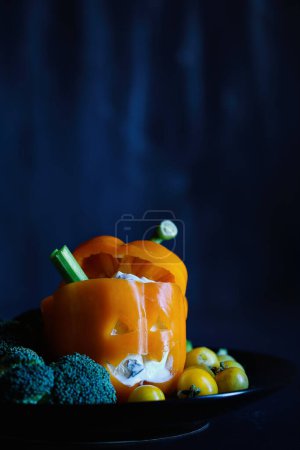 Photo for Colorful stuffed sweet orange bell pepper as monster with cut out face carved into a Halloween pumpkin Jack O'Lantern and filled with Tzatziki dip. Selective focus with blurred foreground and background. - Royalty Free Image
