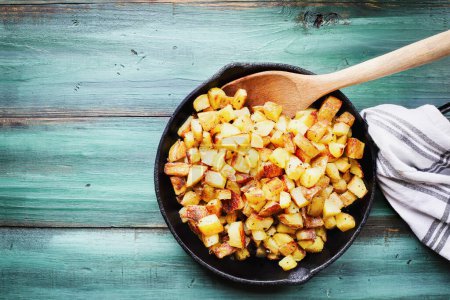 Photo for Table top view of a cast iron skillet filled with fresh crispy golden Yukon gold fried potatoes. Flatlay. Overhead. - Royalty Free Image
