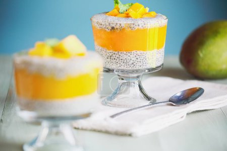Photo for Delicious vegan mango chia pudding with fresh mint springs in a glass jar on a green wooden background. Selective focus with blurred foreground and background. - Royalty Free Image