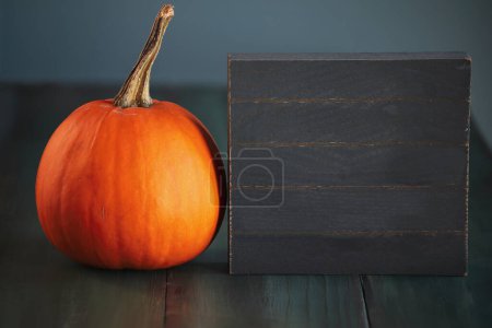 Photo for Autumn blank black wooden sign with orange pumpkin on a green table. Selective focus with blurred foreground and background. - Royalty Free Image