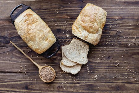 Photo for Above table top view of freshly baked whole wheat bread loaves with wooden spoon filled with grain. Overhead. - Royalty Free Image