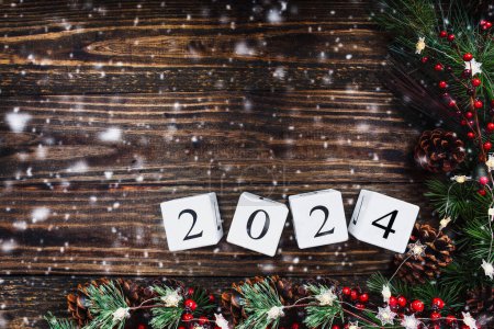 Photo for New Year's 2024 wood calendar blocks. Christmas tree lights, pine branches, red winter berries and snow over wooden table background. Top view with copy space available. - Royalty Free Image