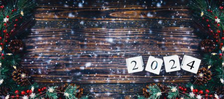 Photo for New Year's 2024 wood calendar blocks banner. Christmas tree lights, pine branches, red winter berries and snow over wooden table background. Top view, flat lay with copy space available. - Royalty Free Image