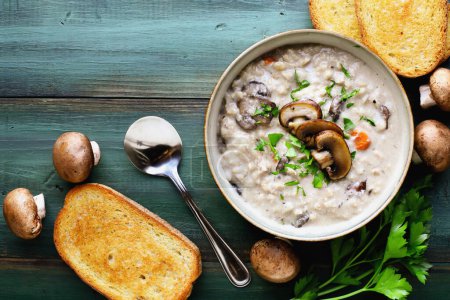 Photo for Mushroom Soup with portobella mushrooms, carrots and fresh parsley. Served with toasted french bread over a green wood table. Table top view. Overhead. - Royalty Free Image