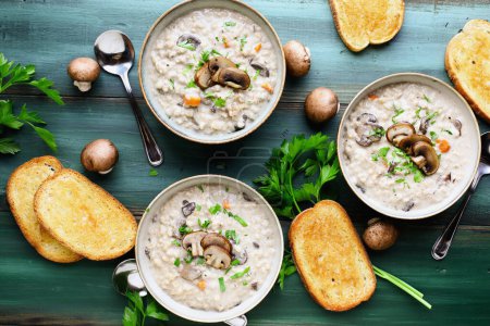 Photo for Three bowls of Mushroom Soup with portobella mushrooms, carrots and fresh parsley. Served with toasted french bread over a green wood table. Table top view. Overhead. - Royalty Free Image