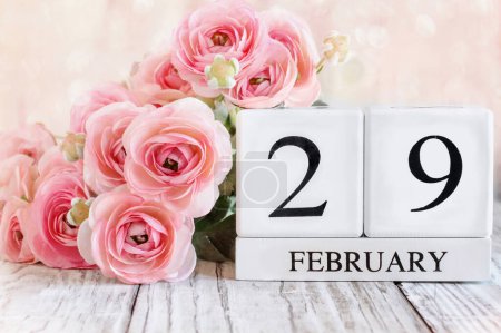 Année bissextile. Des blocs de calendrier en bois blanc avec la date du 29 février et des fleurs de ranunculus roses sur une table en bois. Mise au point sélective avec fond flou. 