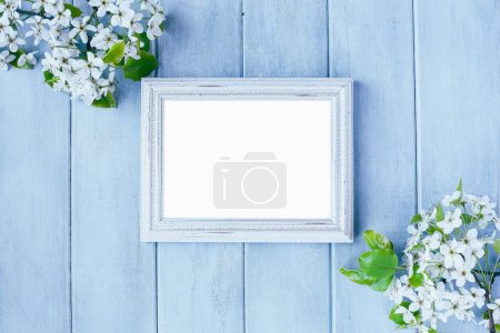Photo for Blank empty rustic white picture frame over blue background with spring flowers. Table top view. - Royalty Free Image