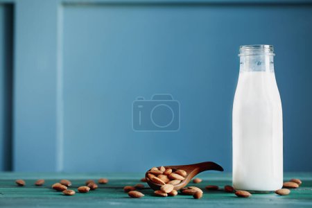 Photo for Whole fresh almonds in a wooden spoon with a bottle of fresh creamy almond white milk over a rustic table or background. Selective focus with blurred background. - Royalty Free Image