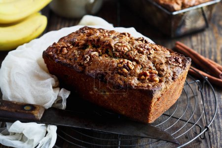 Photo for Overhead view of fresh homemade banana bread cooling on a baker's rack with ingredients nearby. Selective focus on loaf with blurred background - Royalty Free Image