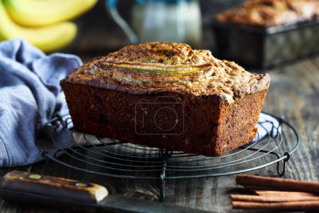 Photo for Front side view of fresh homemade banana bread cooling on a baker's rack with ingredients nearby. Selective focus on loaf with blurred background - Royalty Free Image