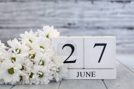 Photo for White wood calendar blocks with the date June 27th and white daisies. Selective focus with blurred background. - Royalty Free Image