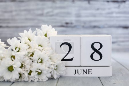 Photo for White wood calendar blocks with the date June 28th and white daisies. Selective focus with blurred background. - Royalty Free Image