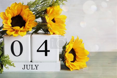 Photo for United States Independence Day. White wood calendar blocks with the date July 4th and beautiful sunflower bouquet with bokeh. Selective focus with blurred background. - Royalty Free Image