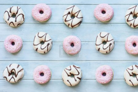 Photo for Flatlay of frosted vanilla donuts with chocolate swirls and strawberry pink doughnuts with coconut flakes. Overhead table top view. Flatlay background. - Royalty Free Image