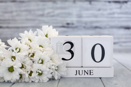 Photo for White wood calendar blocks with the date June 30th and white daisies. Selective focus with blurred background. - Royalty Free Image