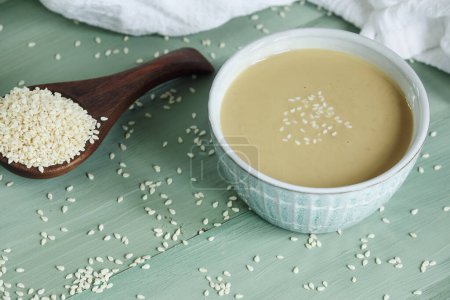 Photo for Top view of pretty bowl filled with tahini sauce. Wooden spoon overflowing with sesame seeds. Top view. - Royalty Free Image