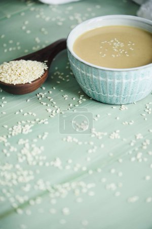 Photo for Pretty bowl filled with tahini sauce with copy space. Wooden spoon overflowing with sesame seeds. Top view. - Royalty Free Image