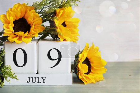 National Sugar Cookie Day. White wood calendar blocks with the date July 9th and beautiful sunflower bouquet with bokeh. Selective focus with blurred background. 