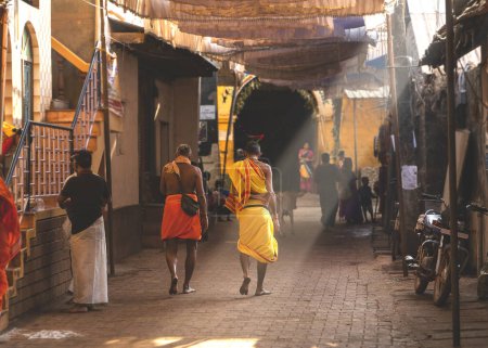Photo for Morning in Gokarna, people walking along a street illuminated by sunlight. Karnataka state, India. - Royalty Free Image