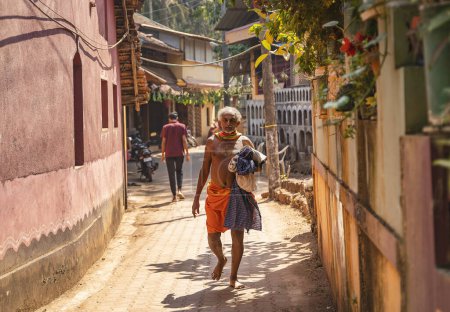 Photo for Gokarna, India - February 21, 2023 - Morning in Gokarna, a man in an orange loincloth walking down the street. - Royalty Free Image