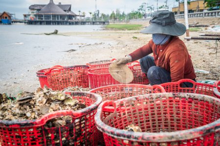 Foto de Vietnam Central, 19 de noviembre de 2022: El pescador está clasificando la captura matutina de almejas en la orilla de la laguna Tam Giang-Cau Hai en Vietnam Central - Imagen libre de derechos