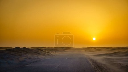 Téléchargez les photos : Conduire sur une route vide dans le désert en Mauritanie au coucher du soleil - en image libre de droit
