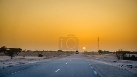 Téléchargez les photos : Conduire à travers un village dans le désert en Mauritanie au coucher du soleil - en image libre de droit