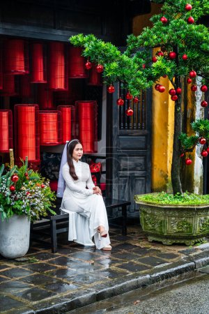 Photo for Hoi An, Vietnam, November 21, 2022: A young woman in a bridal gown is posing for a photo in front of a traditional Vietnamese shop in Hoi An, Vietnam - Royalty Free Image