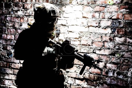 Foto de A silhouette of soldier in action in a ruined building, sneaking in darkness along brick wall. Concept of urban military war conflict - Imagen libre de derechos