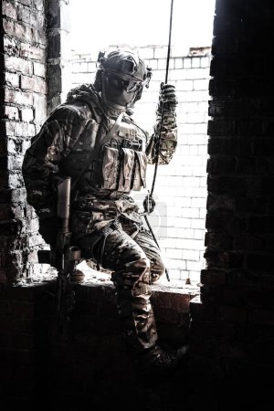 Photo for Black and white image of rappeller - police officer or soldier in tactical gear descending from a height to attack and fight. Tactical rappelling, anti-terror or counter terrorism operation in ruined - Royalty Free Image