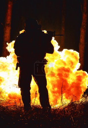 Foto de Silueta retroiluminada de fuerzas especiales operadora marina en bosque sobre fondo de explosión de fuego. Batalla, bombas explotando, pelean sin importar lo que pase - Imagen libre de derechos