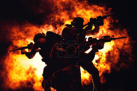 Foto de Silueta retroiluminada de los operadores de fuerzas especiales que luchan en el humo en el fondo de la explosión de fuego. Batalla, bombas explotando, pelean sin importar lo que pase - Imagen libre de derechos