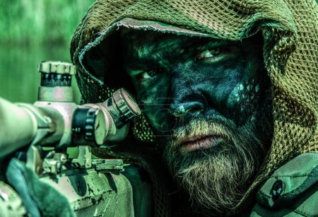 Ein getarnter Soldat mit durchdringendem Blick wacht in taktischer Ausrüstung im Dschungel-Wald-Sumpf. Nahaufnahme Porträt mit Gewehr. 
