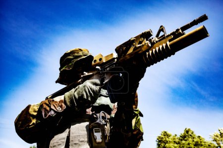 High quality photo Silhouetted against the sky, a soldier in a braced position holds his rifle, ready to shoot. Low angle photo