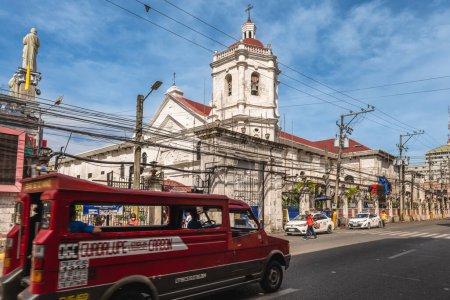 Photo for May 2, 2023: A Jeepney pass by the  Santo Nino Basilica, a minor basilica in Cebu City in the Philippines that was founded in 1565. It is the oldest Roman Catholic church in the country build in 1740. - Royalty Free Image