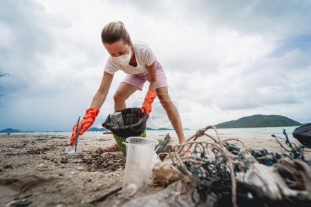 Foto de Una voluntaria ecologista limpia la playa en la orilla del mar de plástico y otros desechos. - Imagen libre de derechos