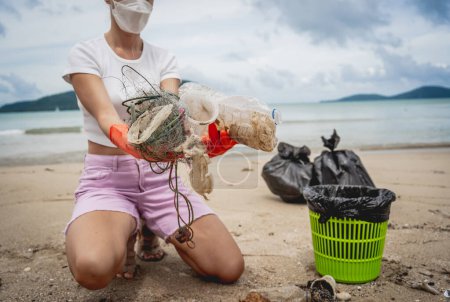 Foto de Una voluntaria ecologista limpia la playa en la orilla del mar de plástico y otros desechos. - Imagen libre de derechos
