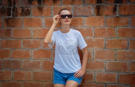 Foto de Modelo femenino con camiseta blanca en blanco en el fondo de una pared de ladrillos - Imagen libre de derechos
