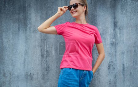 Téléchargez les photos : Modèle féminin portant un t-shirt blanc rose sur le fond d'un mur gris rayé - en image libre de droit