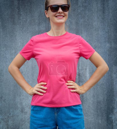 Téléchargez les photos : Modèle féminin portant un t-shirt blanc rose sur le fond d'un mur gris rayé - en image libre de droit