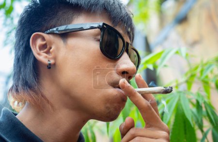 Téléchargez les photos : Jeune homme fumant des cigarettes avec de la marijuana médicale. - en image libre de droit