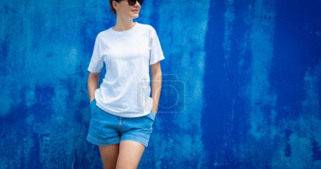 Foto de Modelo femenino con camiseta blanca en blanco en el fondo de una pared azul - Imagen libre de derechos