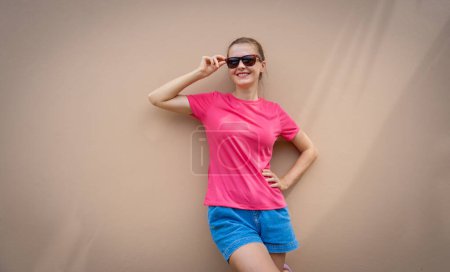 Téléchargez les photos : Modèle féminin portant un t-shirt blanc rose sur le fond d'un mur de sable - en image libre de droit