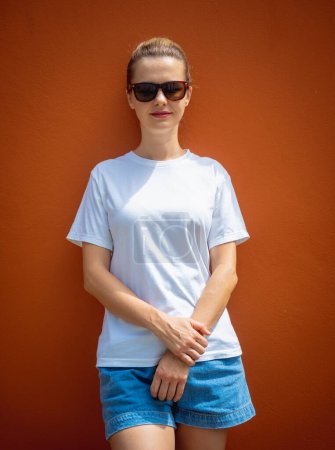 Foto de Modelo femenino con camiseta blanca en blanco en el fondo de una pared naranja - Imagen libre de derechos
