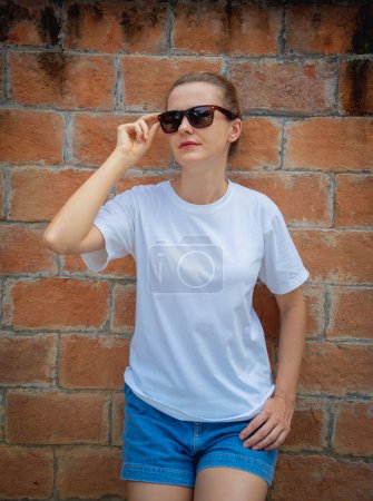 Téléchargez les photos : Modèle féminin portant un t-shirt blanc blanc sur le fond d'un mur de briques - en image libre de droit