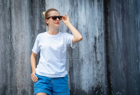 Foto de Modelo femenino con camiseta blanca en blanco en el fondo de una pared gris rayada - Imagen libre de derechos